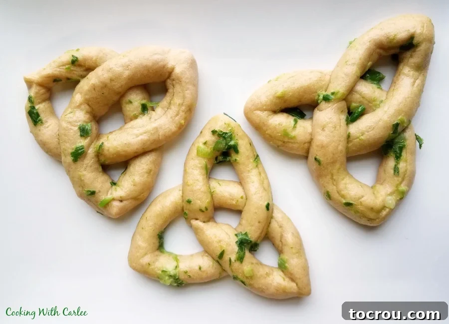 Three Celtic knot bread rolls brushed in herbed butter, ready to eat, beside a bowl of stew.