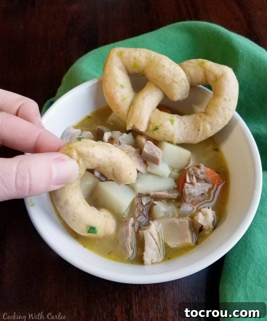 Dipping a freshly baked Celtic knot roll into a warm bowl of easy chicken stew, showcasing its perfect pairing.