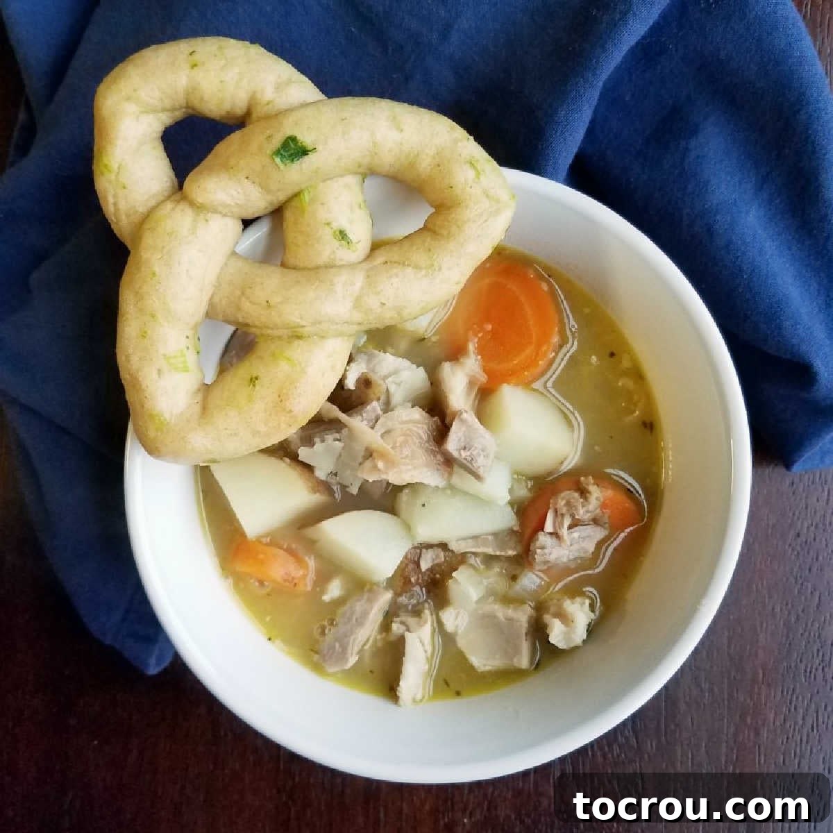 A hearty bowl of chicken stew accompanied by a beautifully shaped trinity knot roll, ready to be enjoyed.