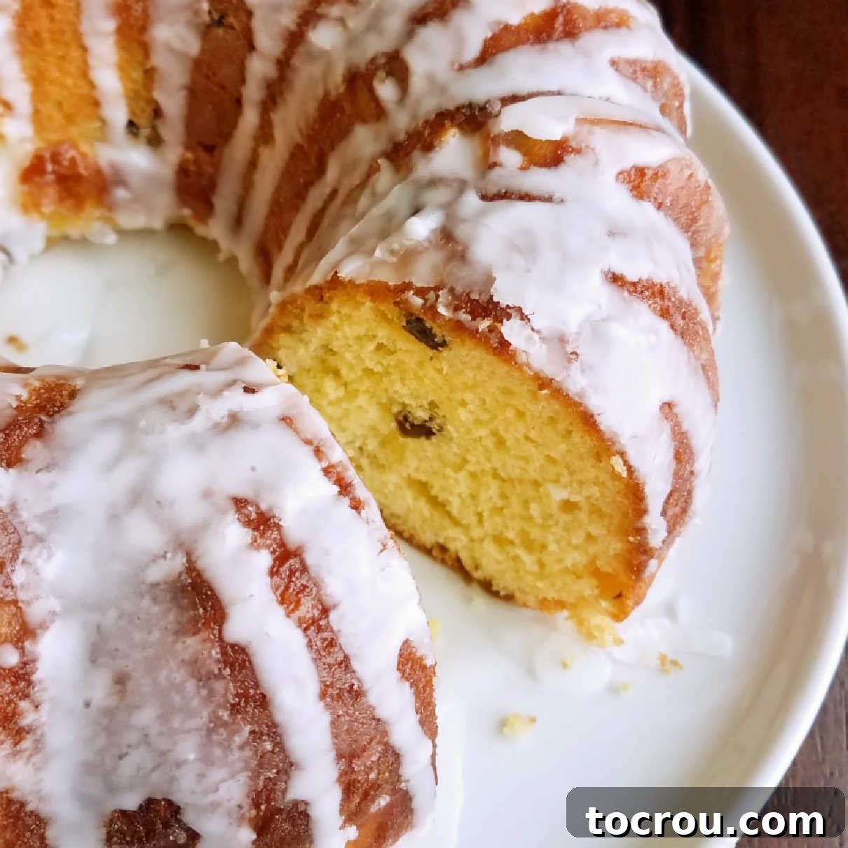 Round loaf of lemon babka with a white glaze missing one slice showing yellow airy lemony center with dots of raisins.