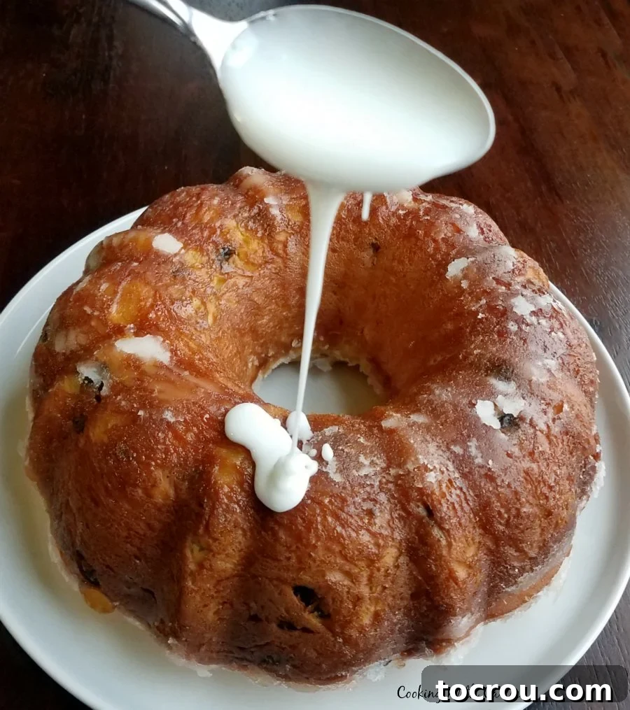 Spoon drizzling powdered sugar glaze over babka on plate.