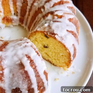 Round loaf of lemon babka with a white glaze missing one slice showing yellow airy lemony center with dots of raisins.