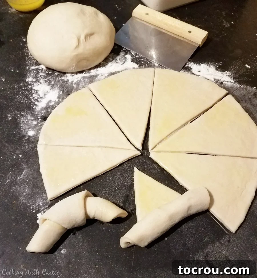 Sourdough crescent dough expertly rolled out into a perfect circle and cut into wedges, with two already shaped into elegant crescent forms.