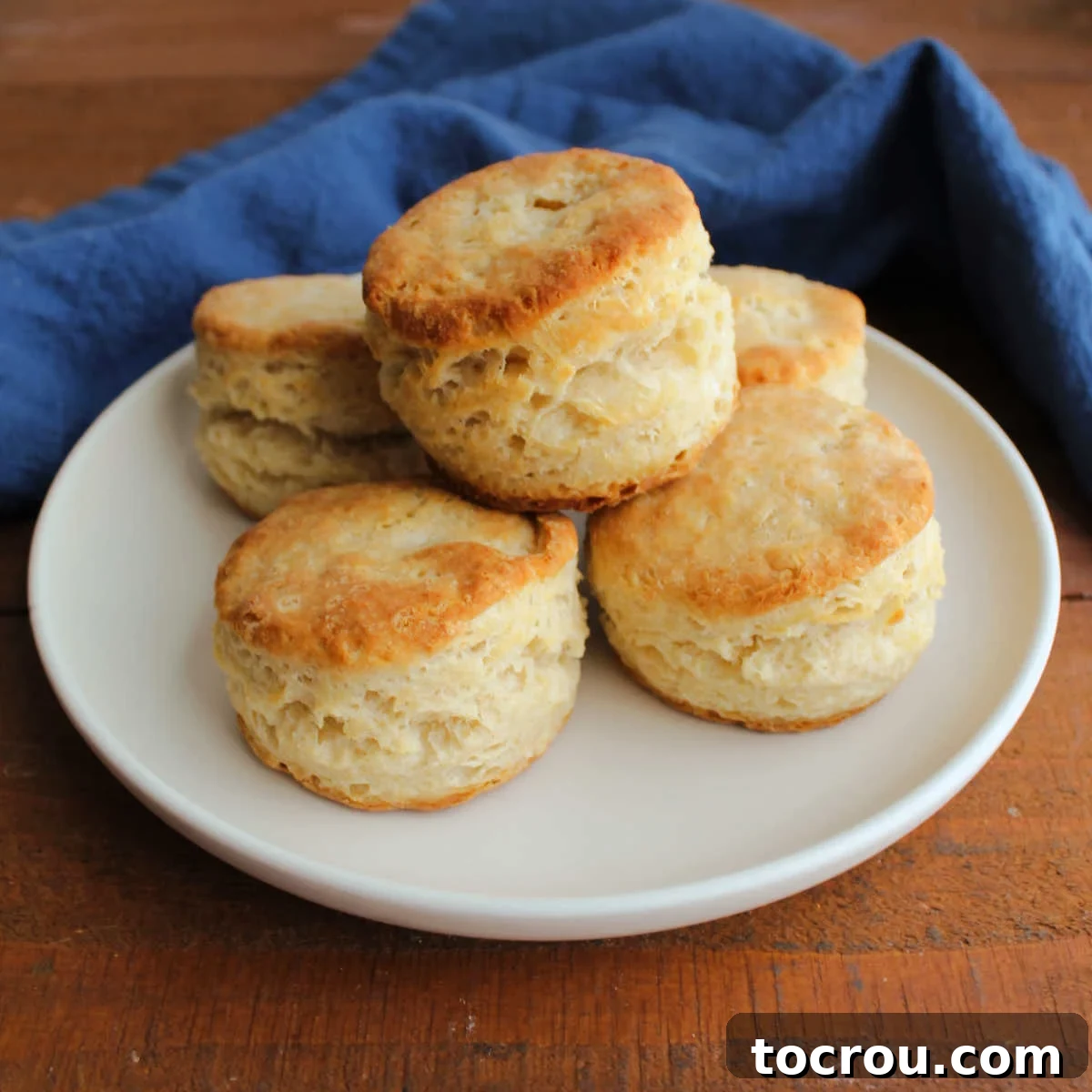 Plate of fluffy, buttery biscuits with golden brown tops and lots of layers. Close up shot showcasing the flaky texture.