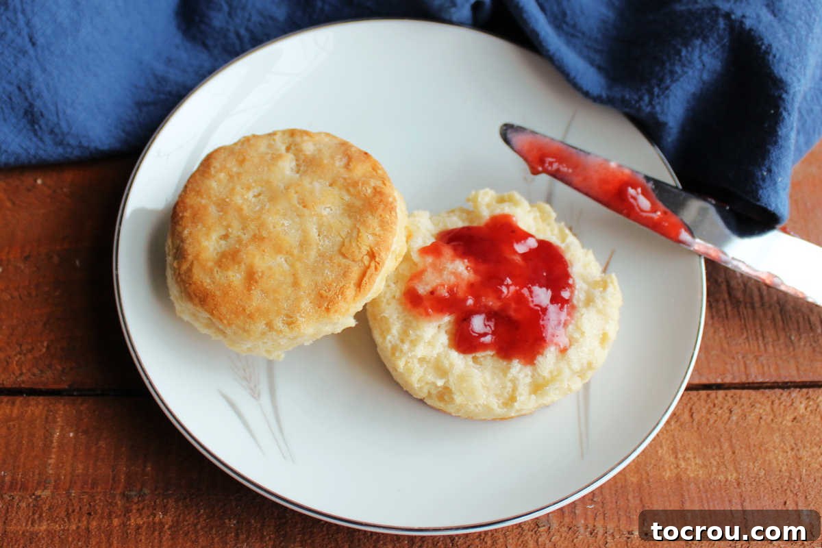 Small plate with a biscuit torn in half with strawberry preserves on the bottom half and it golden buttery top next to it. Ready to be enjoyed.