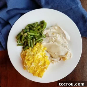 A dinner plate featuring a serving of golden scalloped corn casserole alongside roasted turkey, rich gravy, and crisp green beans, showcasing a classic holiday meal.