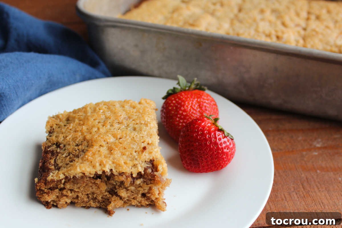 Square of soft oatmeal cake with coconut topping served with a couple of fresh strawberries. 
