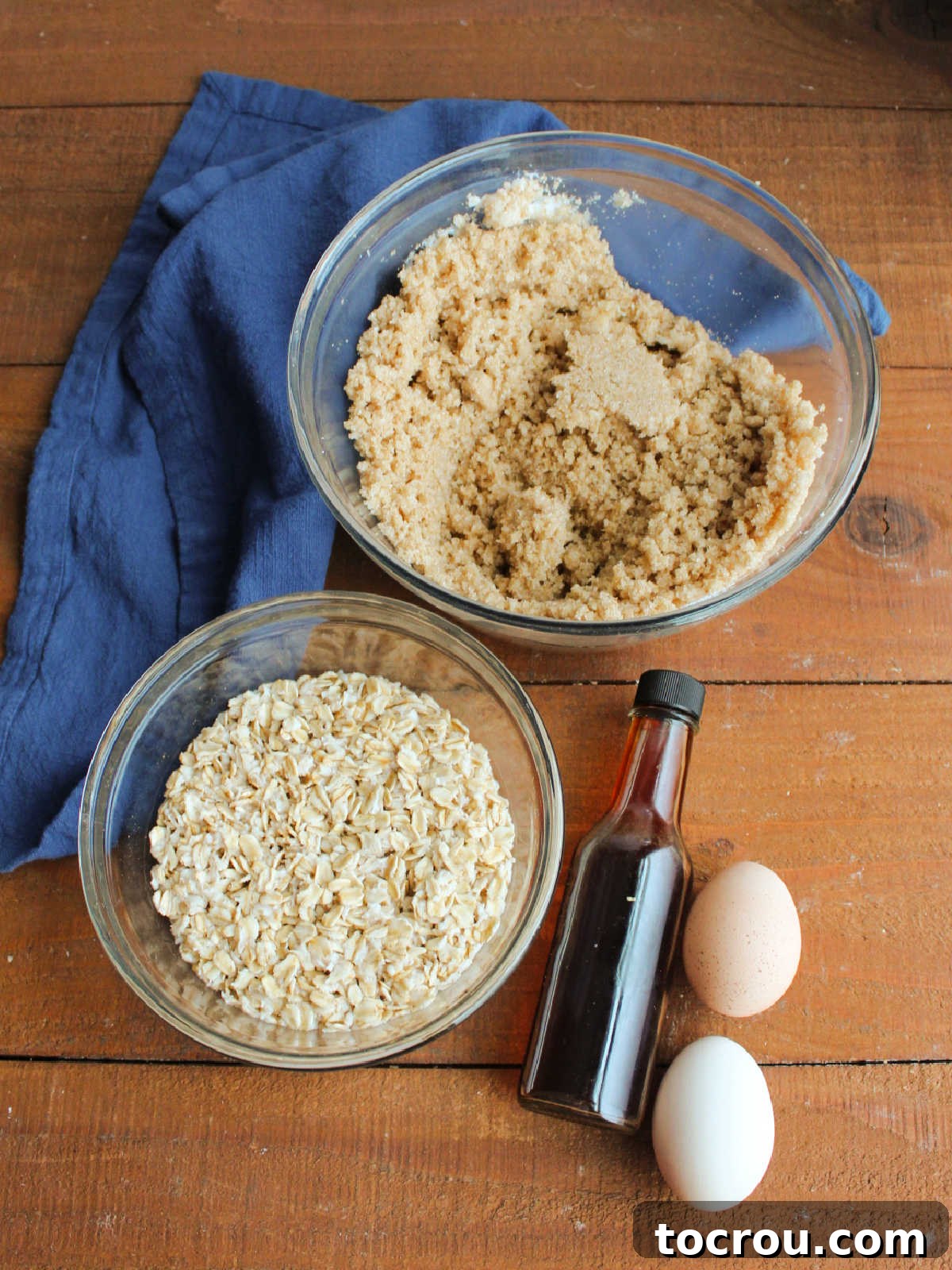 Bowl with soaking oatmeal next to bowl of butter and sugar, with eggs and vanilla for the wet ingredient part of the oatmeal cake batter. 