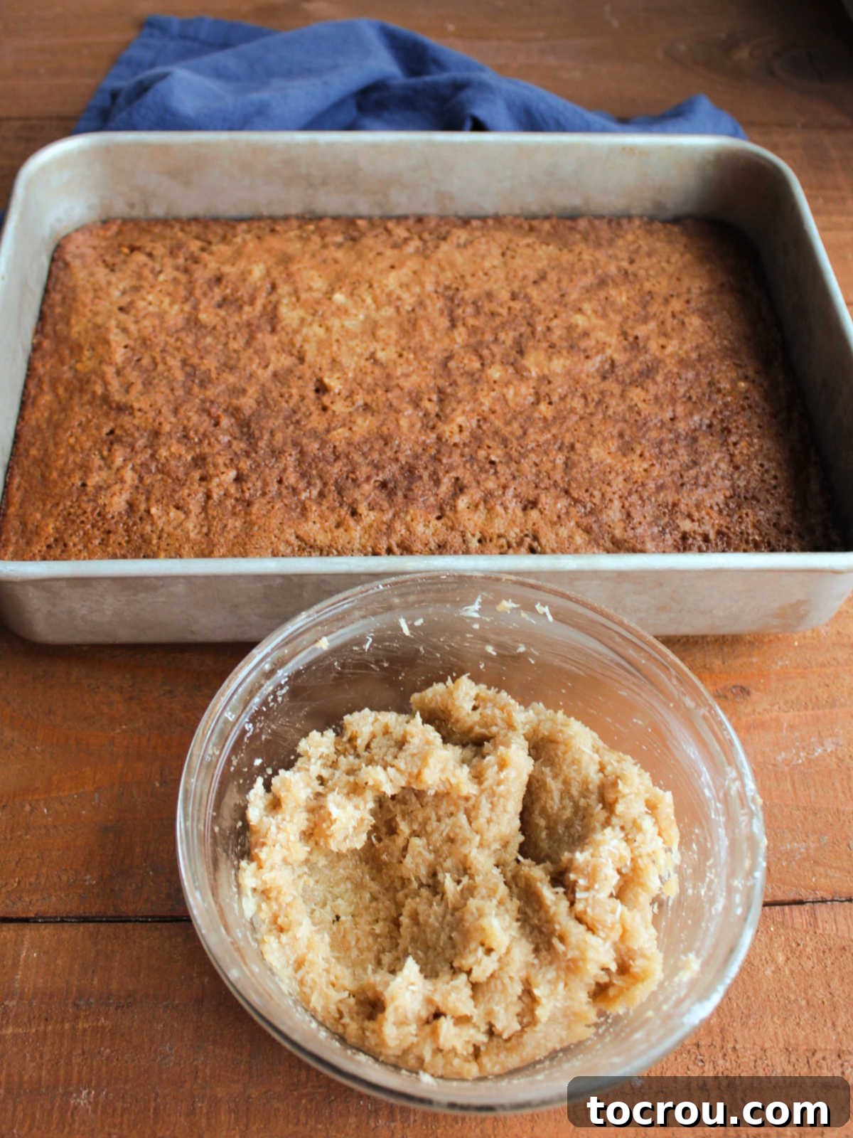 Bowl with coconut and brown sugar topping mixture next to pan with baked cake. 