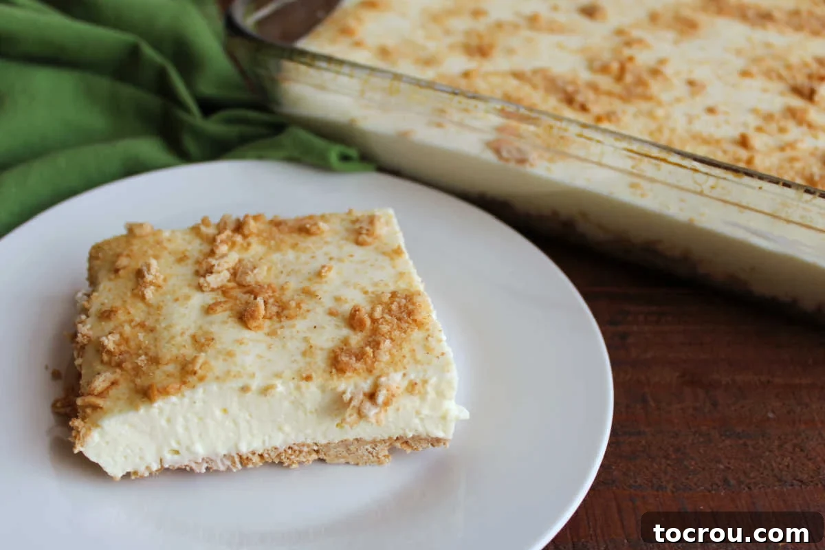 Square piece of no bake woolworth cheesecake on plate showing pale yellow color and creamy texture with graham cracker crust and graham cracker crumbs on top.