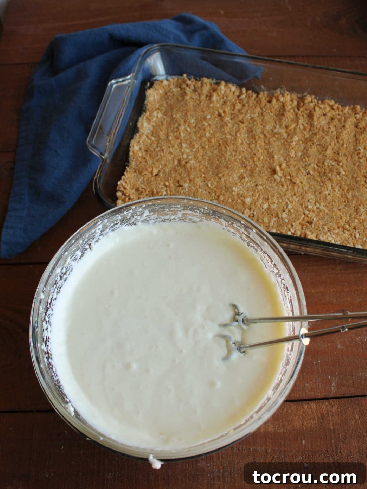 Woolworth no bake cheesecake mixture text to 9x13-inch pan with graham cracker crust inside, ready to be assembled.