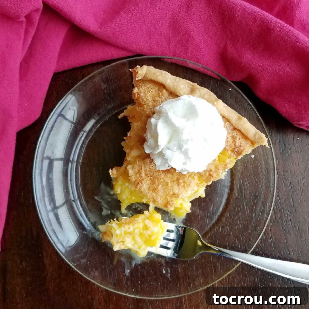 Slice of pineapple coconut pie topped with a dollop of whipped cream, showcasing its golden crust and creamy filling.