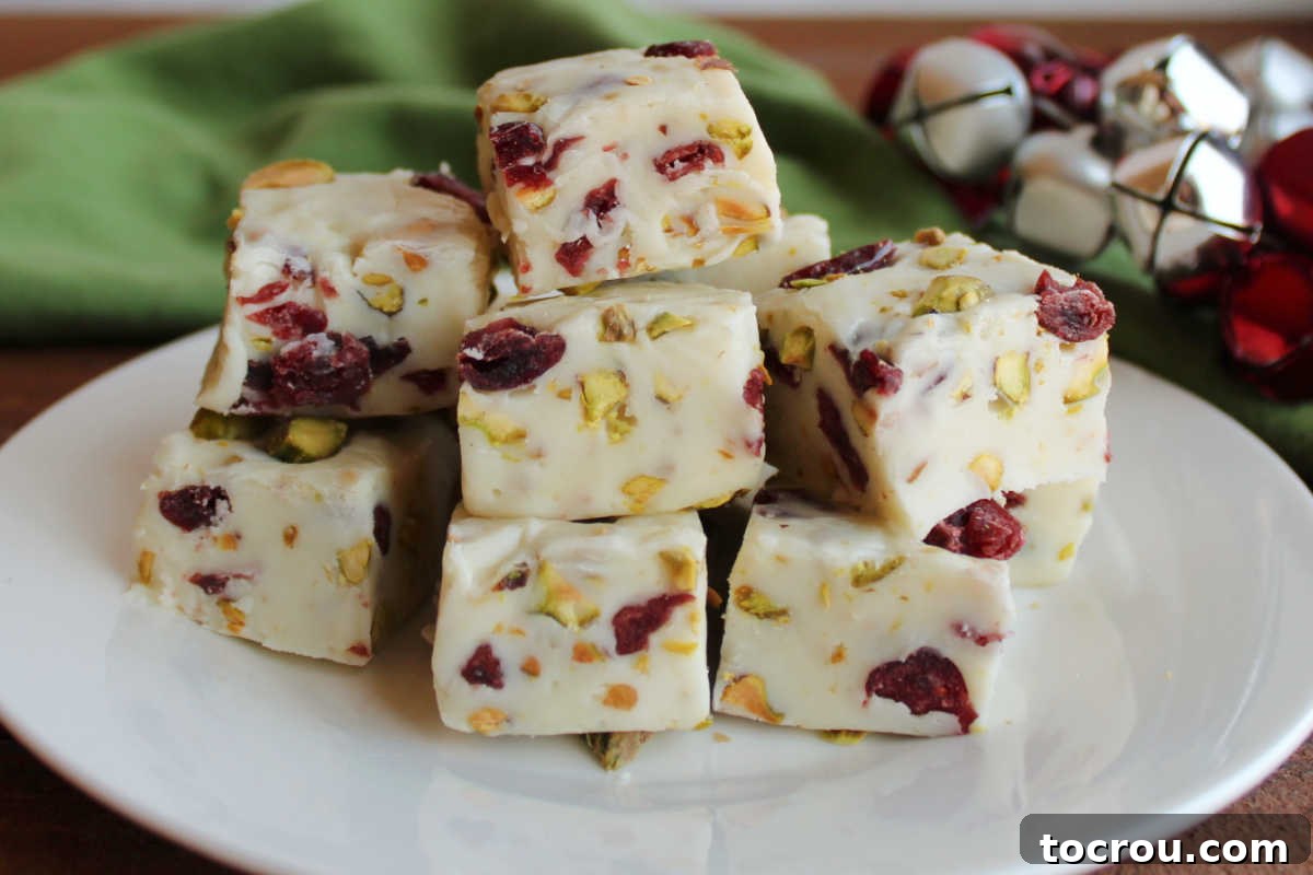 Plate filled with cubes of white vanilla fudge with red and green specs from craisins and pistachios, ready to eat. 