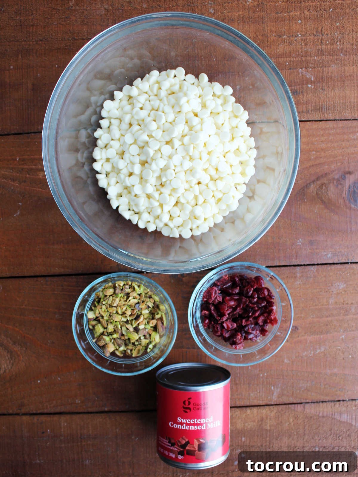 Ingredients including white chocolate chips, craisins, pistachio pieces, and sweetened condensed milk ready to be made into fudge. 