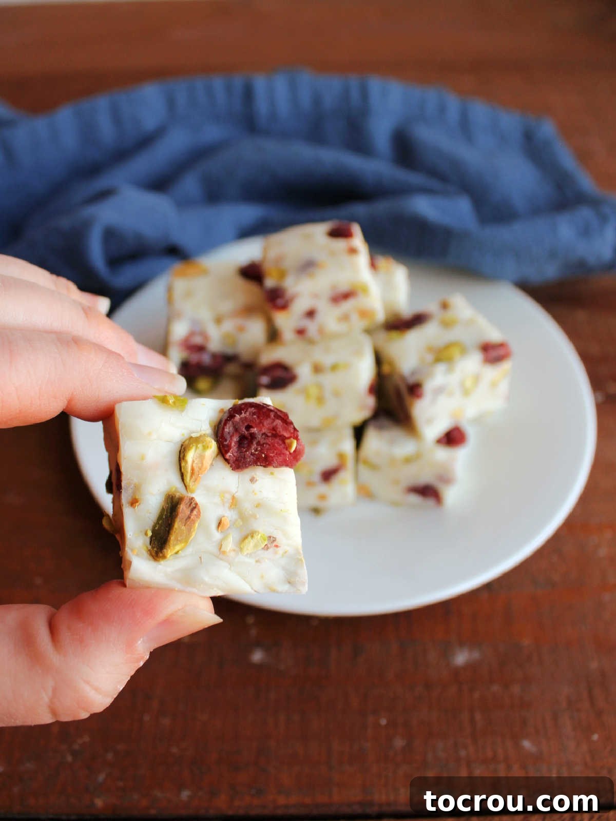 Hand holding piece of white fudge with pieces of pistachio and dried cranberry on top. 