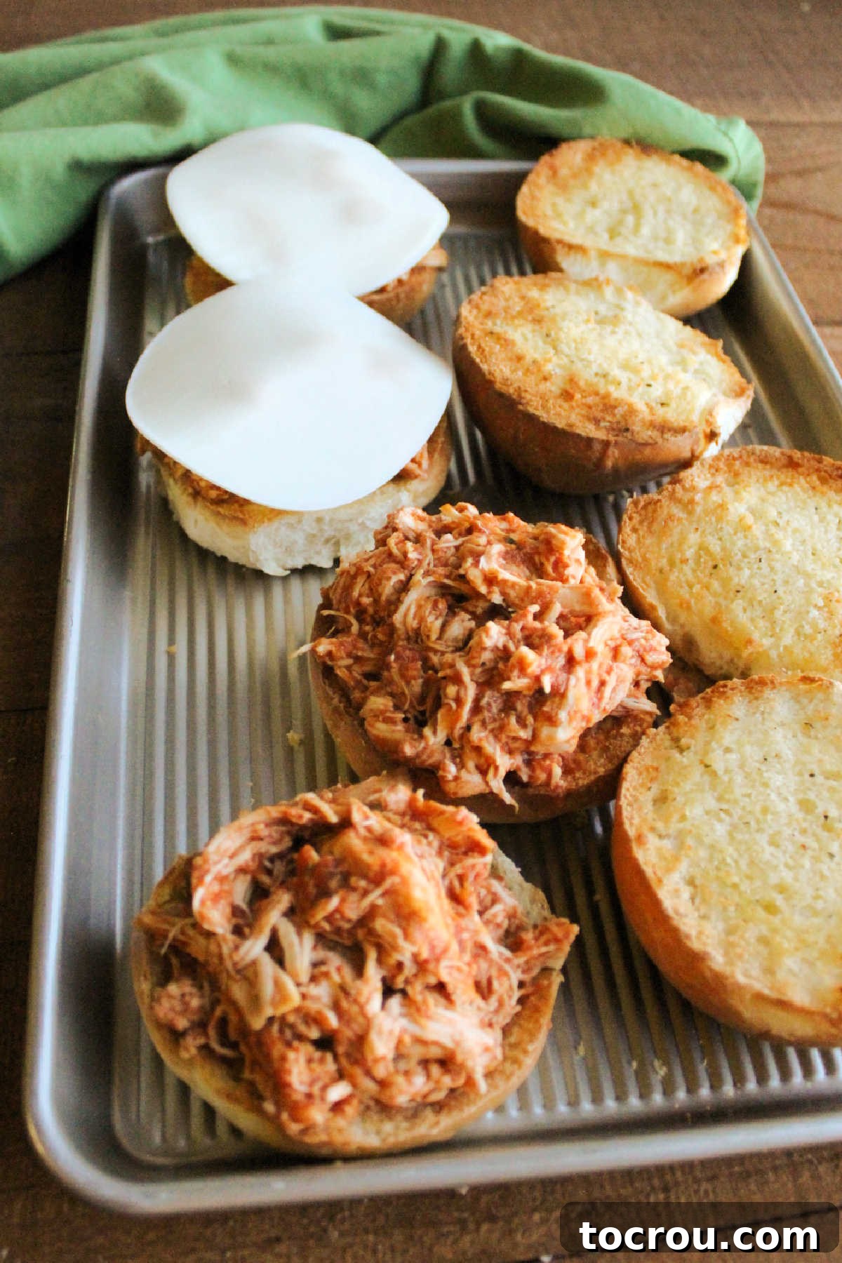 Ready to melt: chicken parmesan on garlic buns with cheese. Toasted garlic buns with shredded chicken and provolone cheese, ready for the oven.