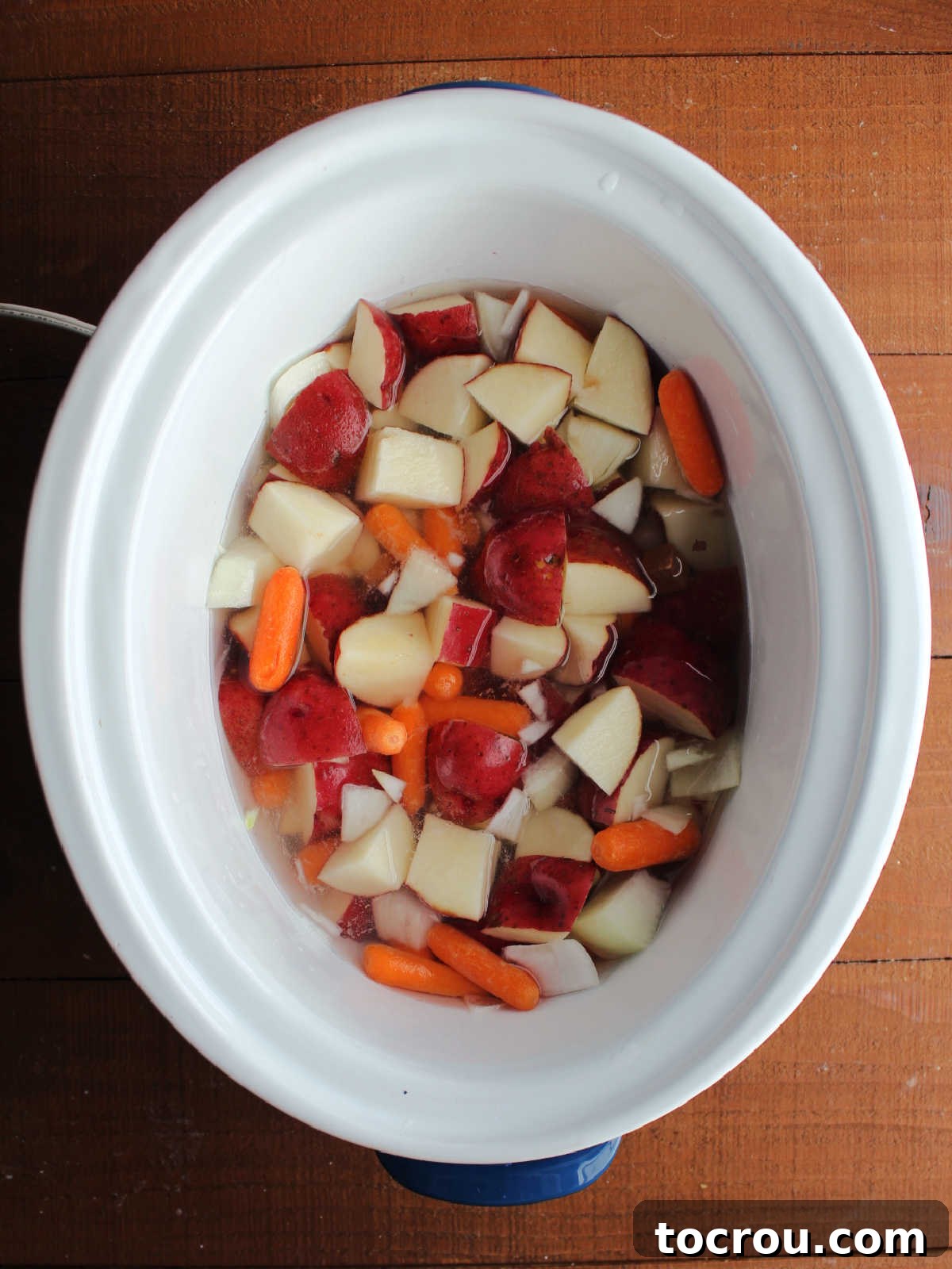 Potatoes, onion, and carrots in crockpot with water. 