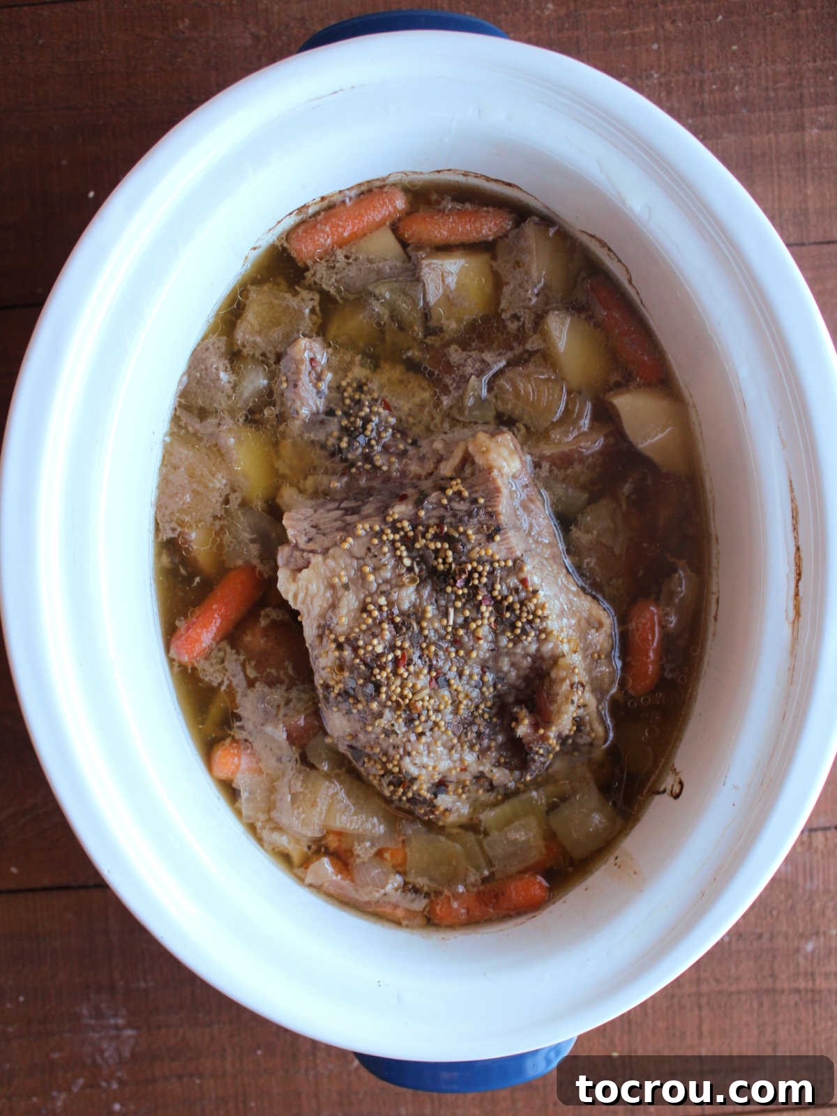 Partially cooked corned beef with potatoes, carrots, onions, and broth in crockpot. 