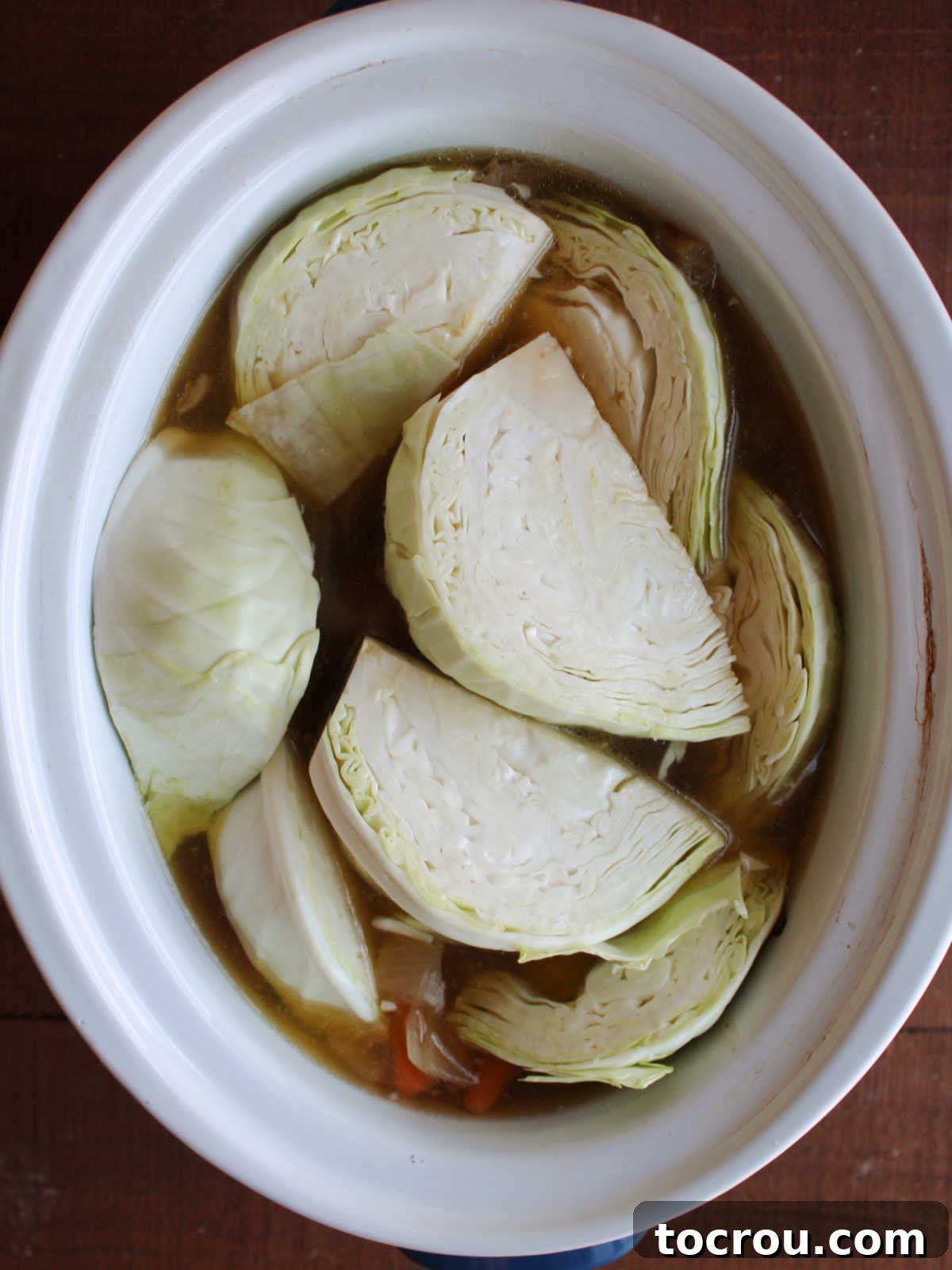 Wedges of cabbage being added to the crockpot with corned beef to cook. 