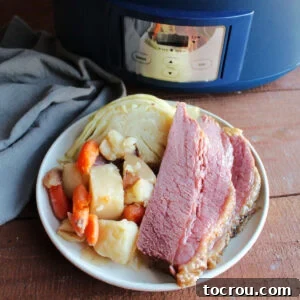 Plate of sliced corned beef with cooked potatoes, carrots, and cabbage wedge by the crockpot it was cooked in.