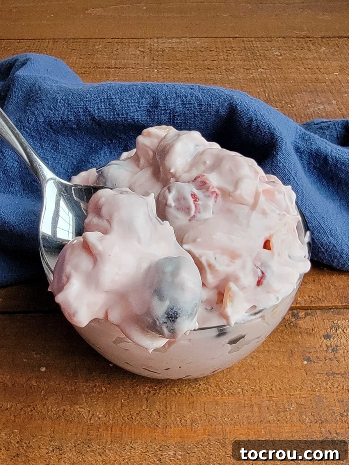 Bite of junk yard salad on spoon showing blueberry and cherries in creamy pink fluff mixture. 