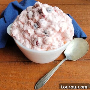 Vintage bowl filled with creamy junk yard fruit salad with cherries, pineapple, marshmallows, and blueberries in pink fluff.