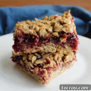 Two sourdough breakfast bars stacked, revealing the luscious raspberry jam filling between the rustic sourdough and oat crusts.