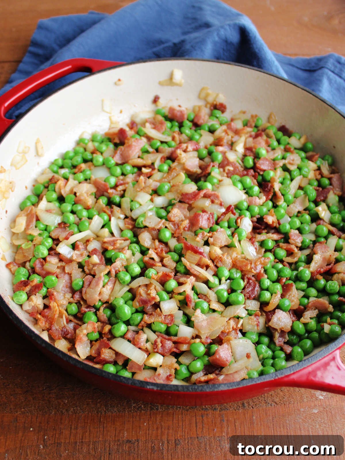 Sautéing Bacon, Onion, and Peas Large pan filled with bits of cooked bacon, diced onion, and peas.