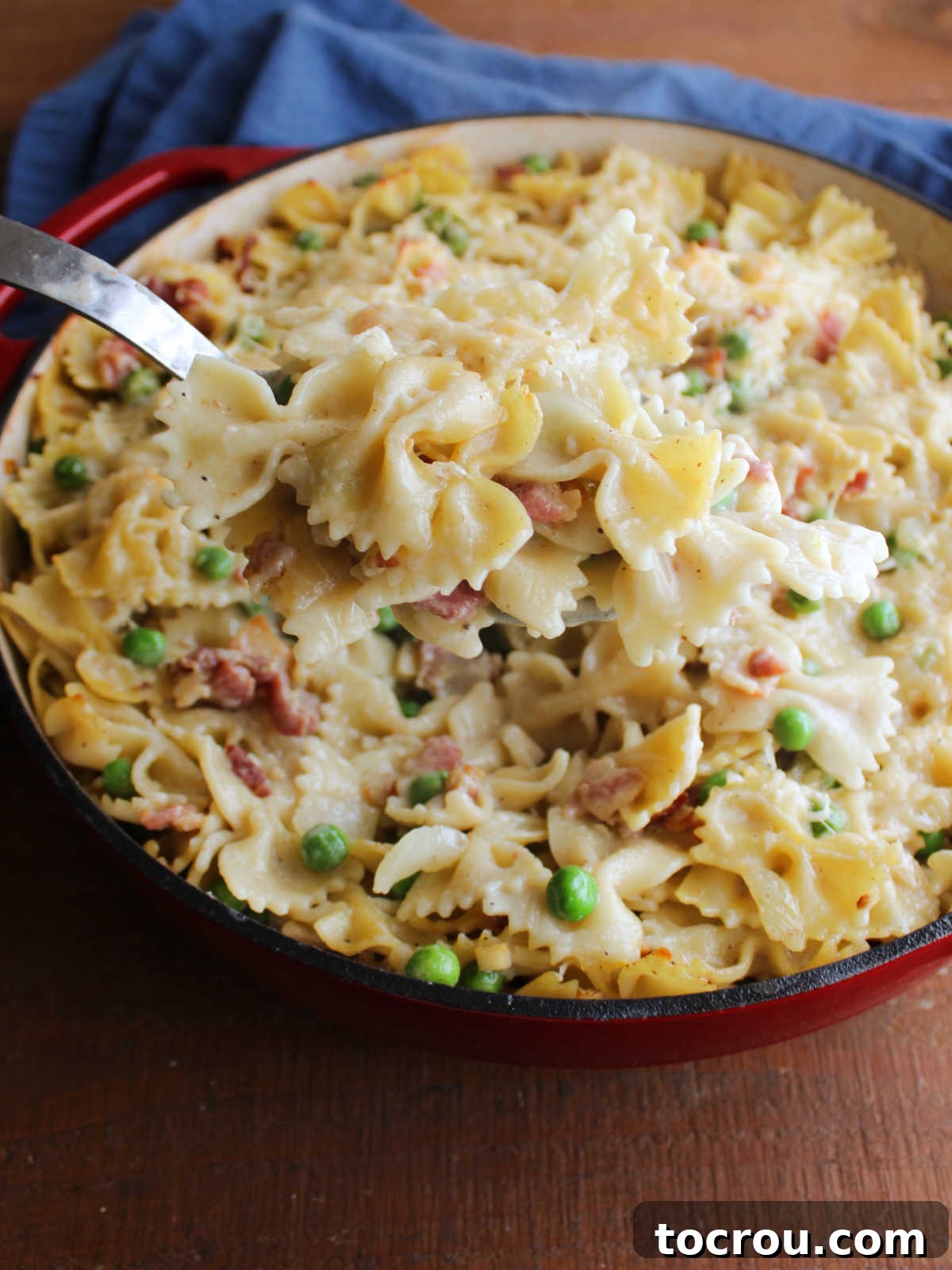 Scooping Baked Pasta Serving spoon lifting out a scoop of baked pasta with alfredo sauce, parmesan cheese, peas, and bacon.