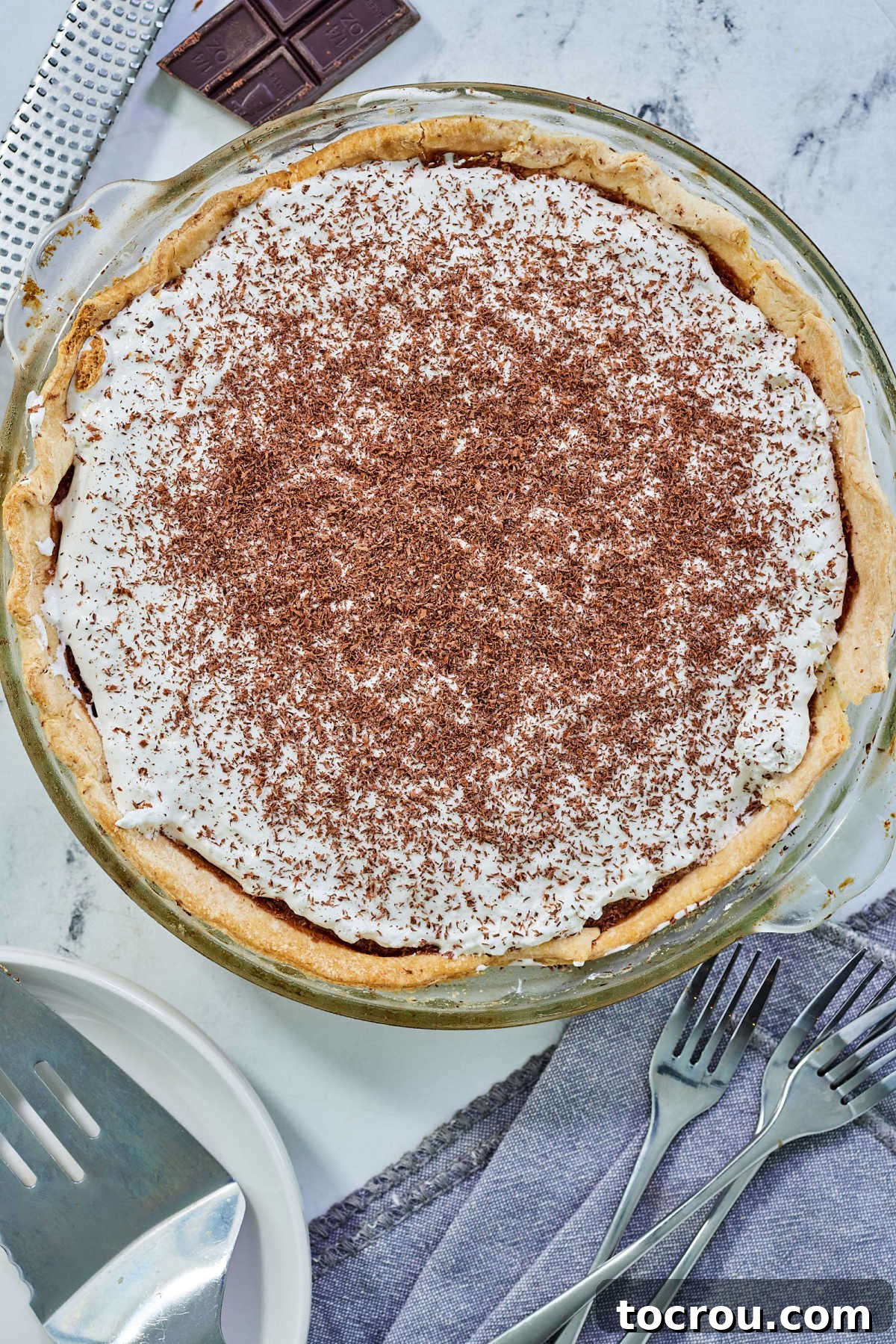 The complete French silk pie, gorgeously adorned with a high swirl of fresh whipped cream and an artful sprinkle of delicate chocolate shavings, impeccably ready for slicing and serving as a truly delightful dessert.