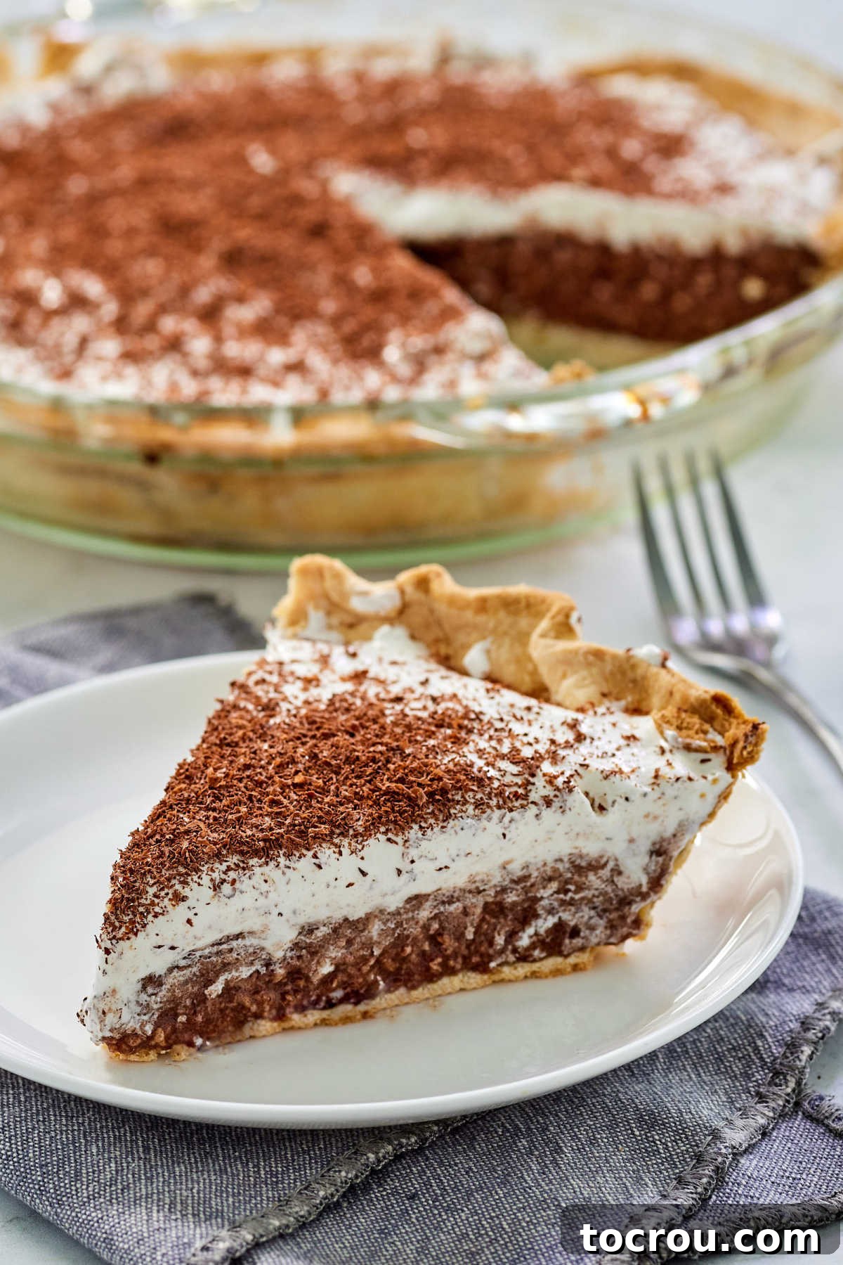 A stunning close-up of a perfectly cut slice of French silk pie, revealing its airy yet richly dense chocolate filling, crowned with a light, fluffy layer of whipped cream, and elegant chocolate shavings. The inviting textures promise pure decadence.