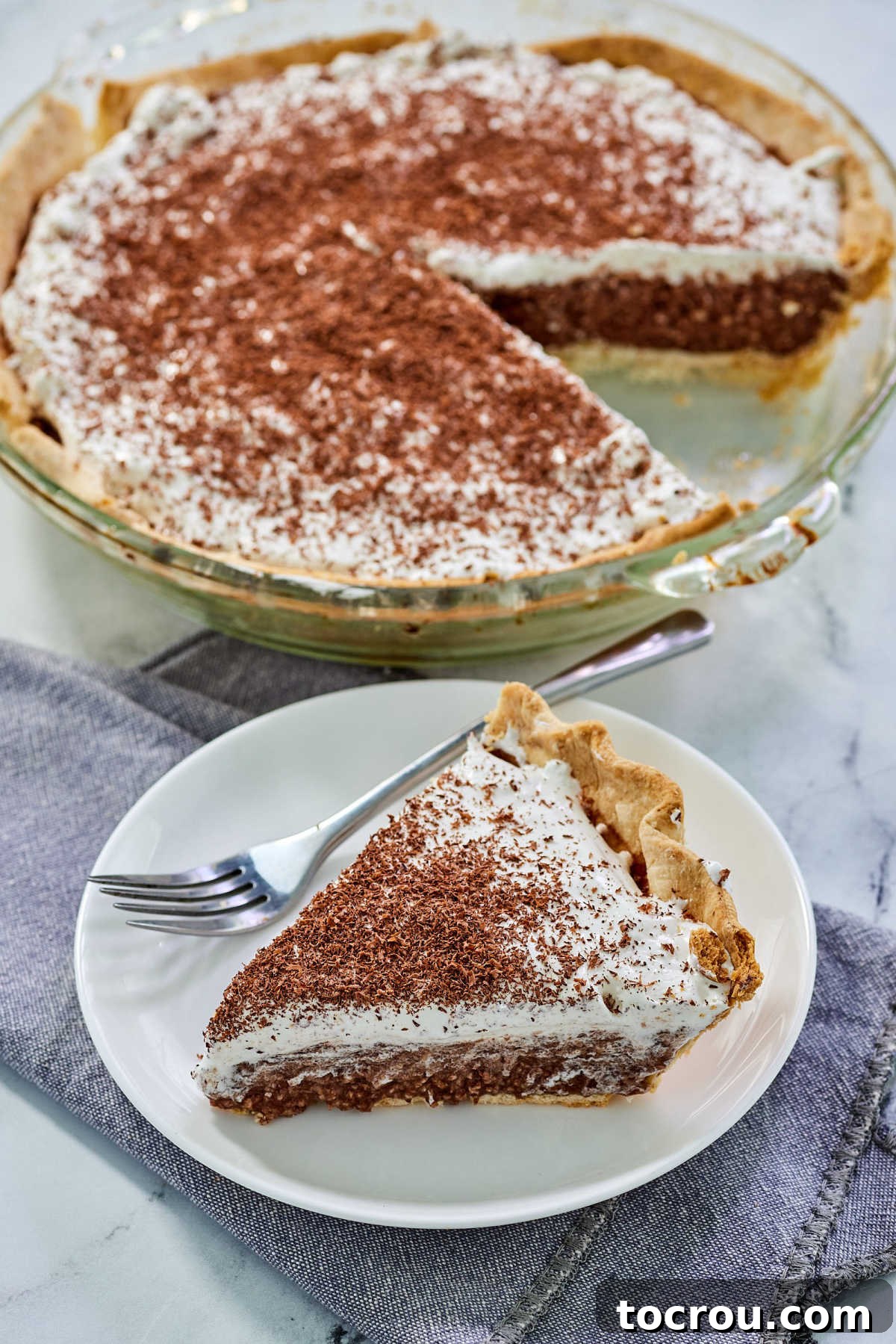 A single slice of homemade French silk pie served on a pristine white dessert plate with a fork poised for tasting, invitingly presented.