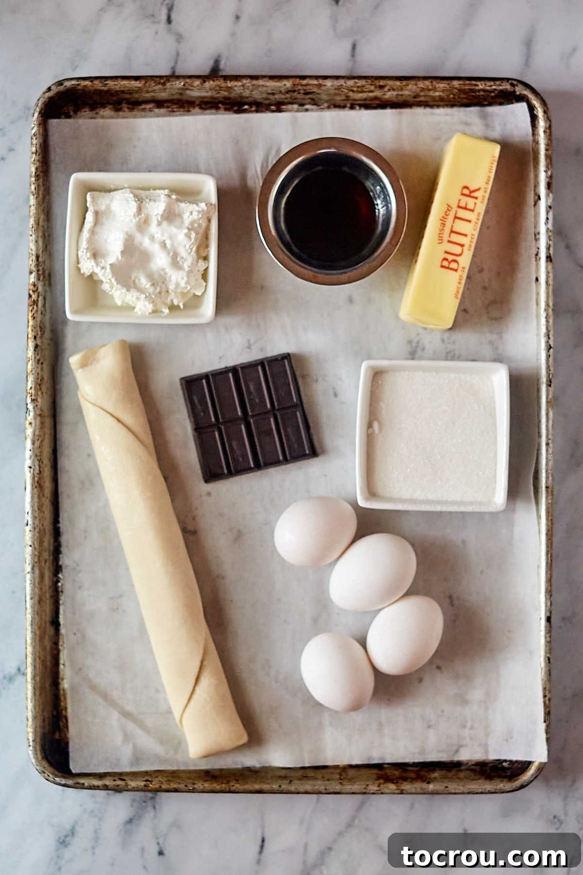 Key ingredients for a perfect French silk pie laid out on a counter: a pre-baked pie crust, fresh eggs, softened unsalted butter, granulated sugar, dark unsweetened chocolate, and pure vanilla extract.