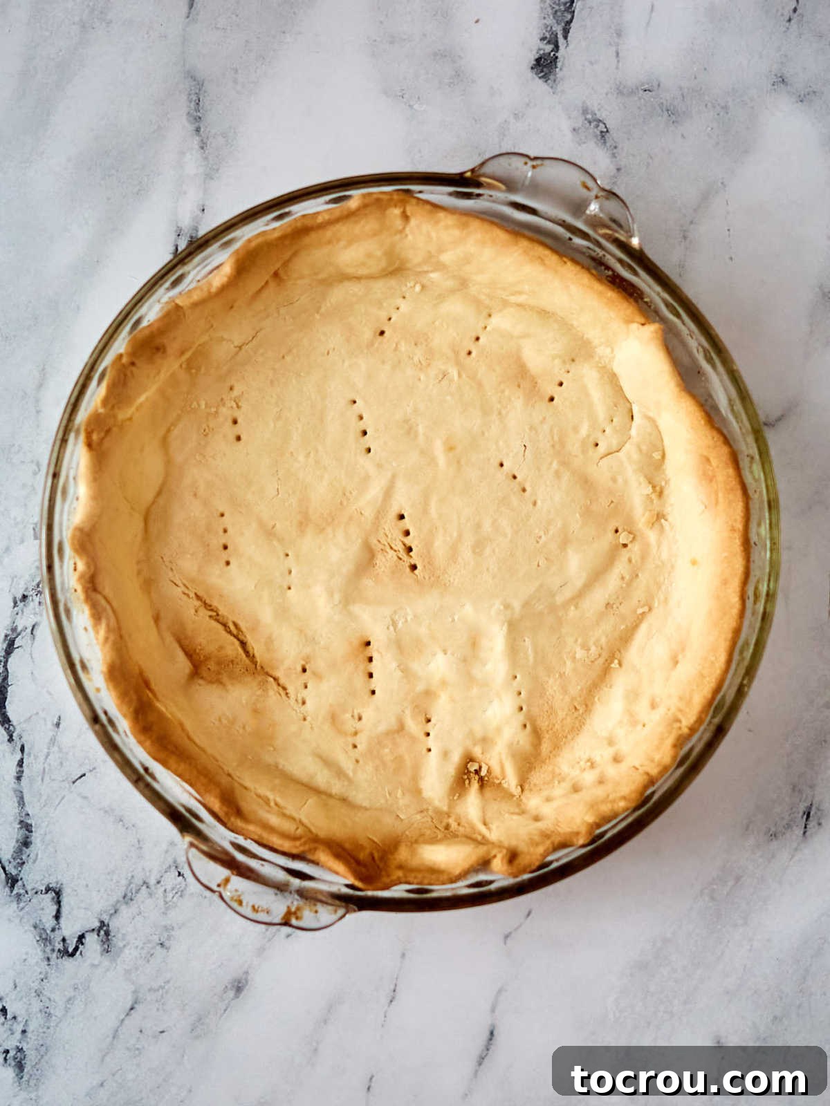 A perfectly golden brown, uniformly baked pie crust resting within a clear glass pie plate, having cooled to perfection and now ready to receive the luscious chocolate filling.