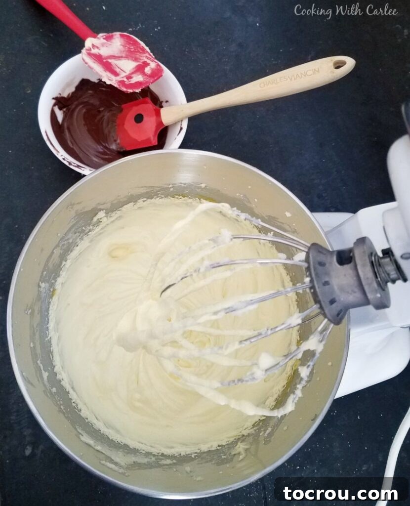 A stand mixer bowl filled with the luscious, creamy mixture of butter, sugar, and vanilla, with a small bowl of perfectly melted and cooled dark chocolate positioned nearby, ready for seamless incorporation into the French silk pie filling.