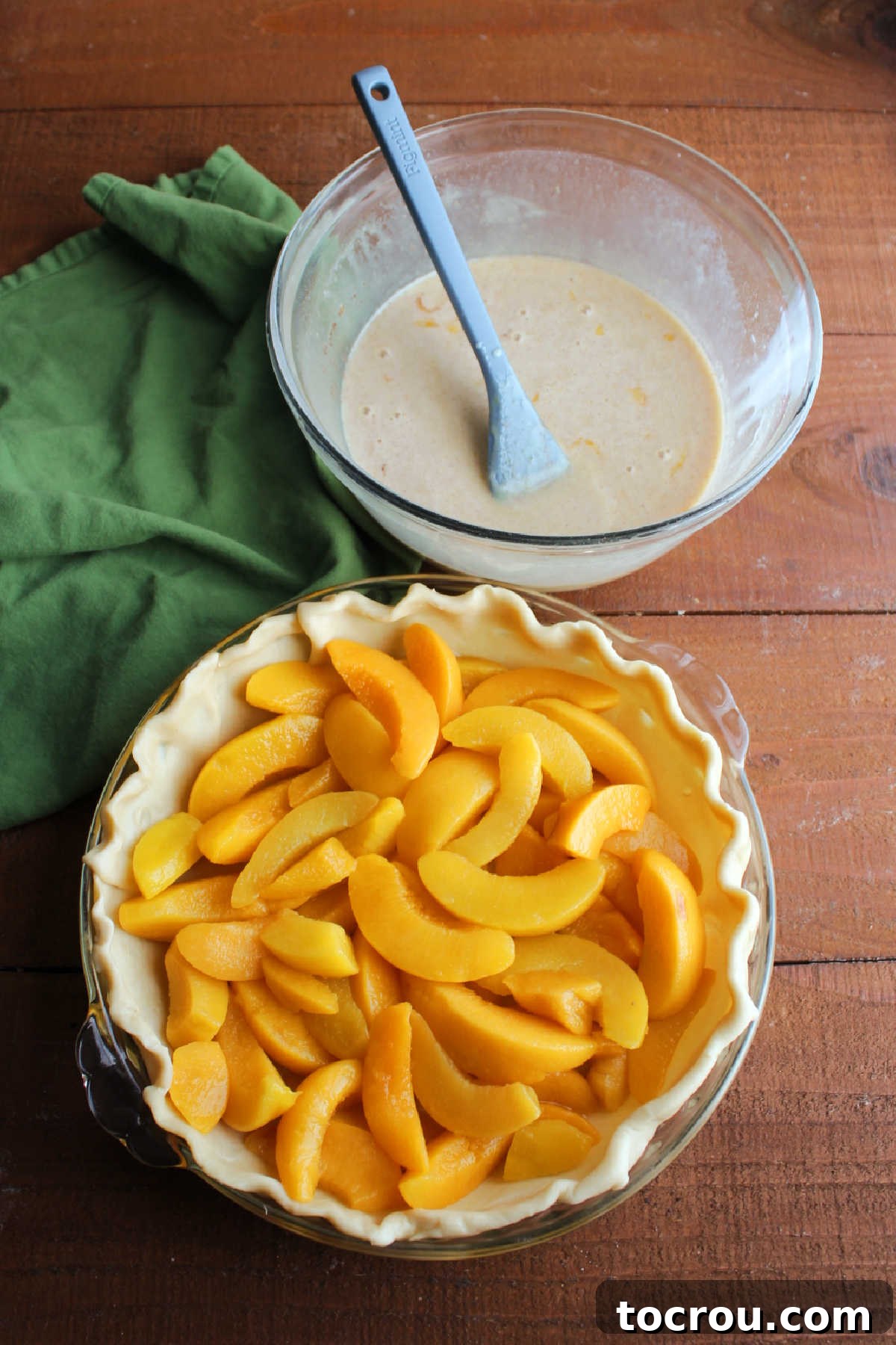 Prepping Peaches and Custard for Pie Defrosted peach slices in pie crust with bowl of sweetened condensed milk custard with cinnamon nearby, ready to go in pie shell.