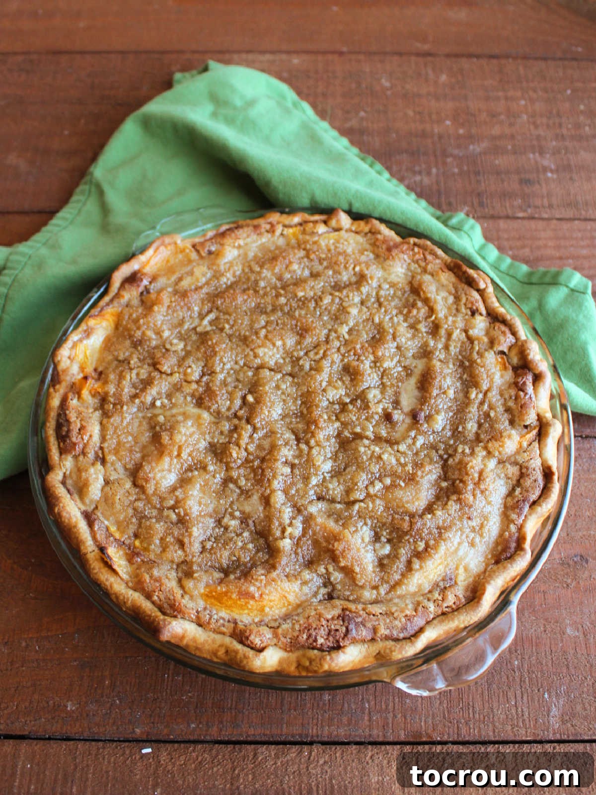 Freshly Baked Peach Custard Pie Baked peach custard pie with golden brown crumb topping and browned pie crust, ready to cool.