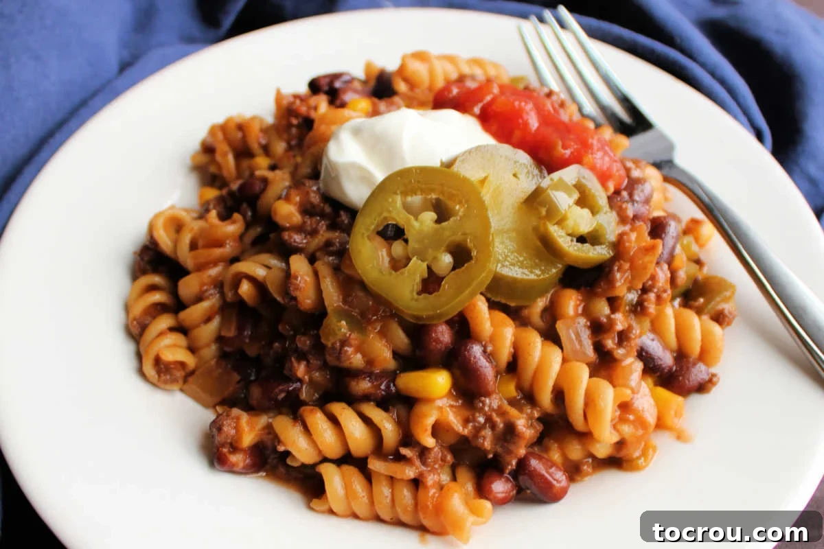 Close up of taco pasta with beans and corn topped with jalapenos, sour cream, and salsa, ready to eat.