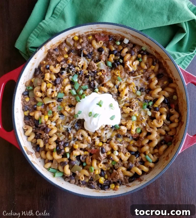 Pot filled with cooked pasta with taco seasoning, ground beef, and veggies topped with cilantro and sour cream.