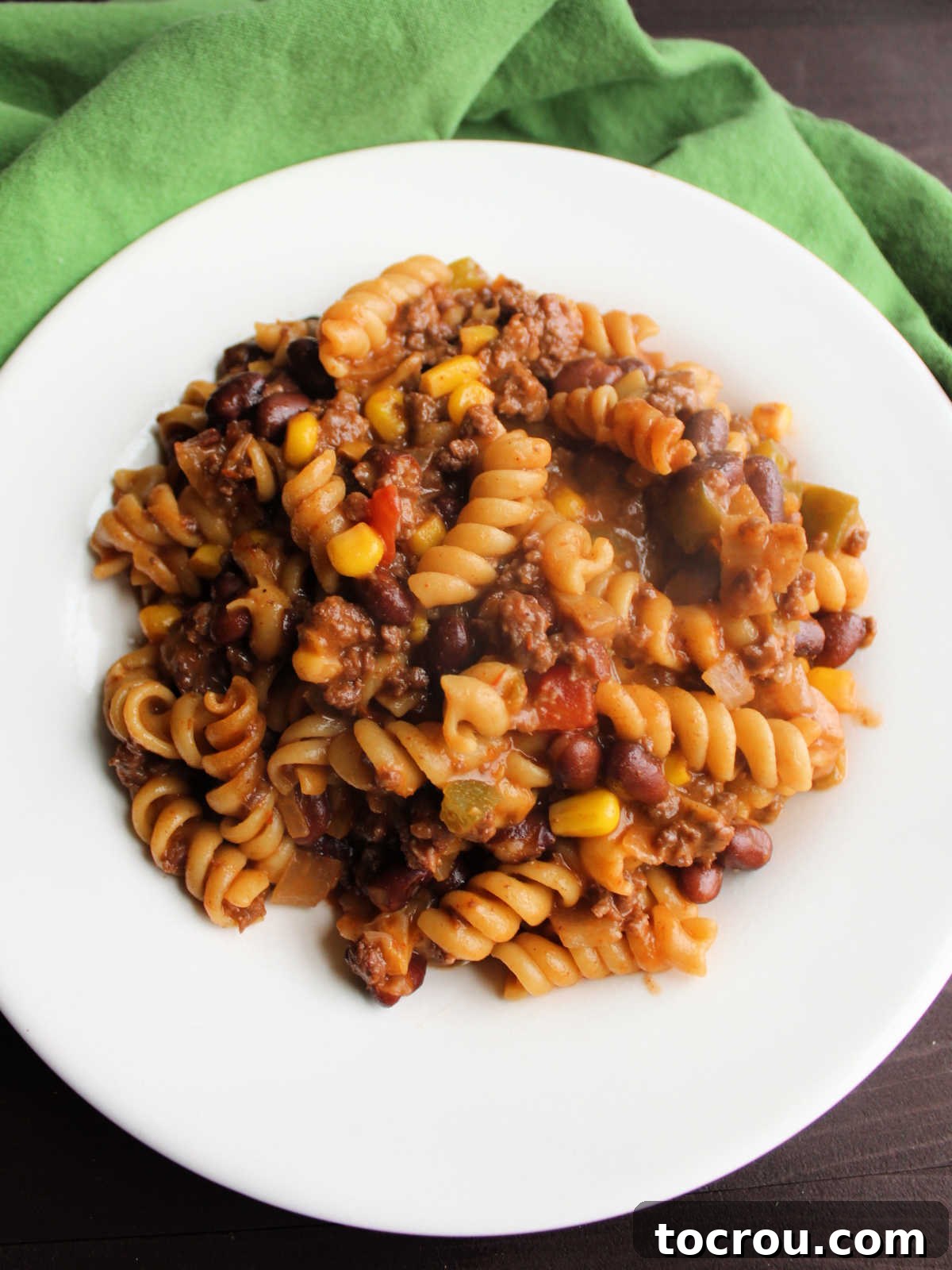 Plate of cooked one pot taco pasta with rotini, ground beef, black beans, corn and more in seasoned sauce.
