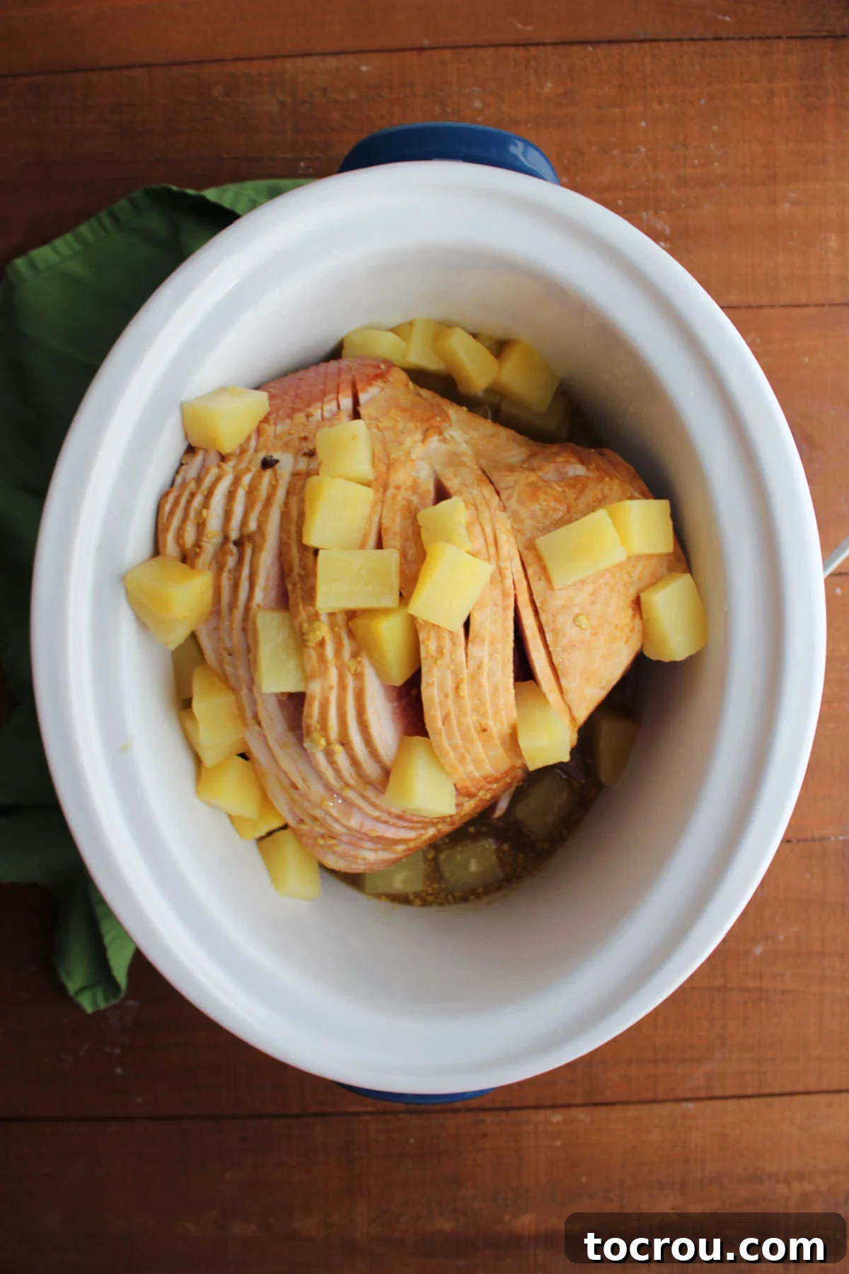 Golden Pineapple Glazed Slow Cooker Ham 4 Spiral ham in crockpot with chunks of pineapple between some of the slices of ham and the sauce poured over everything, ready to cook.