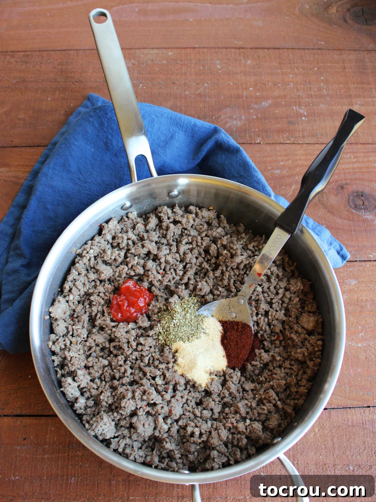 Skillet filled with browned ground beef and sausage mixture with ketchup and seasonings on top, being made into hanky panky dip.
