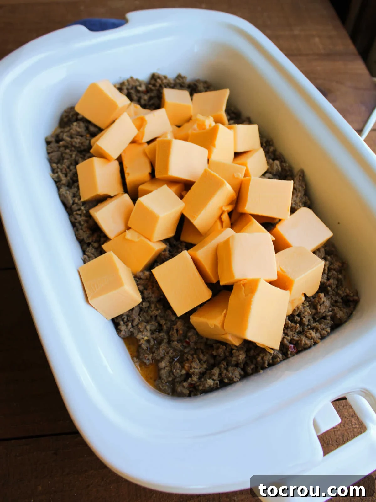 Crockpot with seasoned sausage and hamburger mixture inside topped with cubes of velveeta to be melted in order to make hanky panky dip.