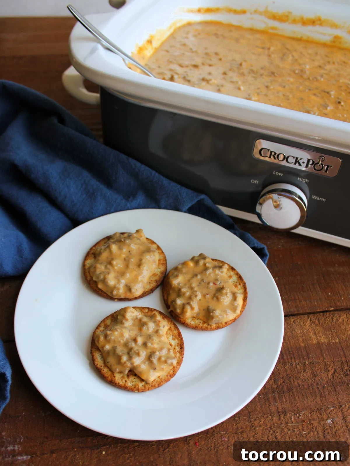 Plate of crackers topped with cheesy hanky panky dip next to a crockpot with more dip inside.