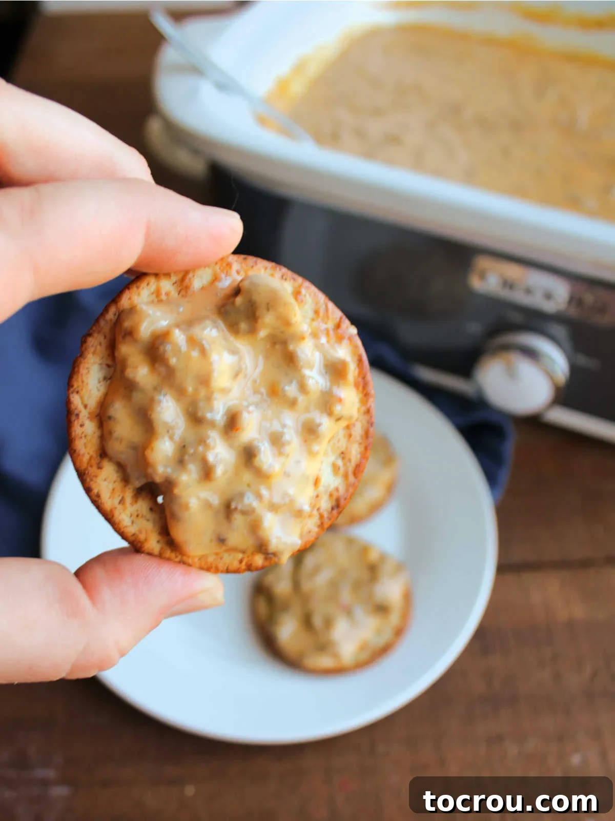 Hand holding a cracker topped with gooey hanky panky dip, ready to eat.