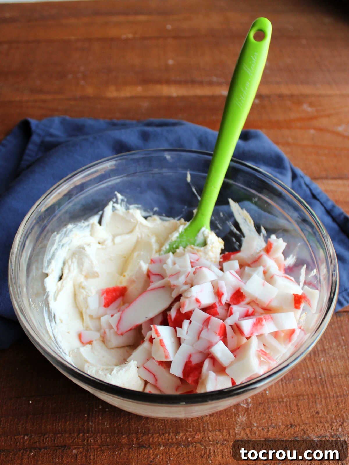 Mixing Crab into Cream Cheese Filling Adding finely chopped imitation crab meat to the seasoned cream cheese mixture in a bowl.