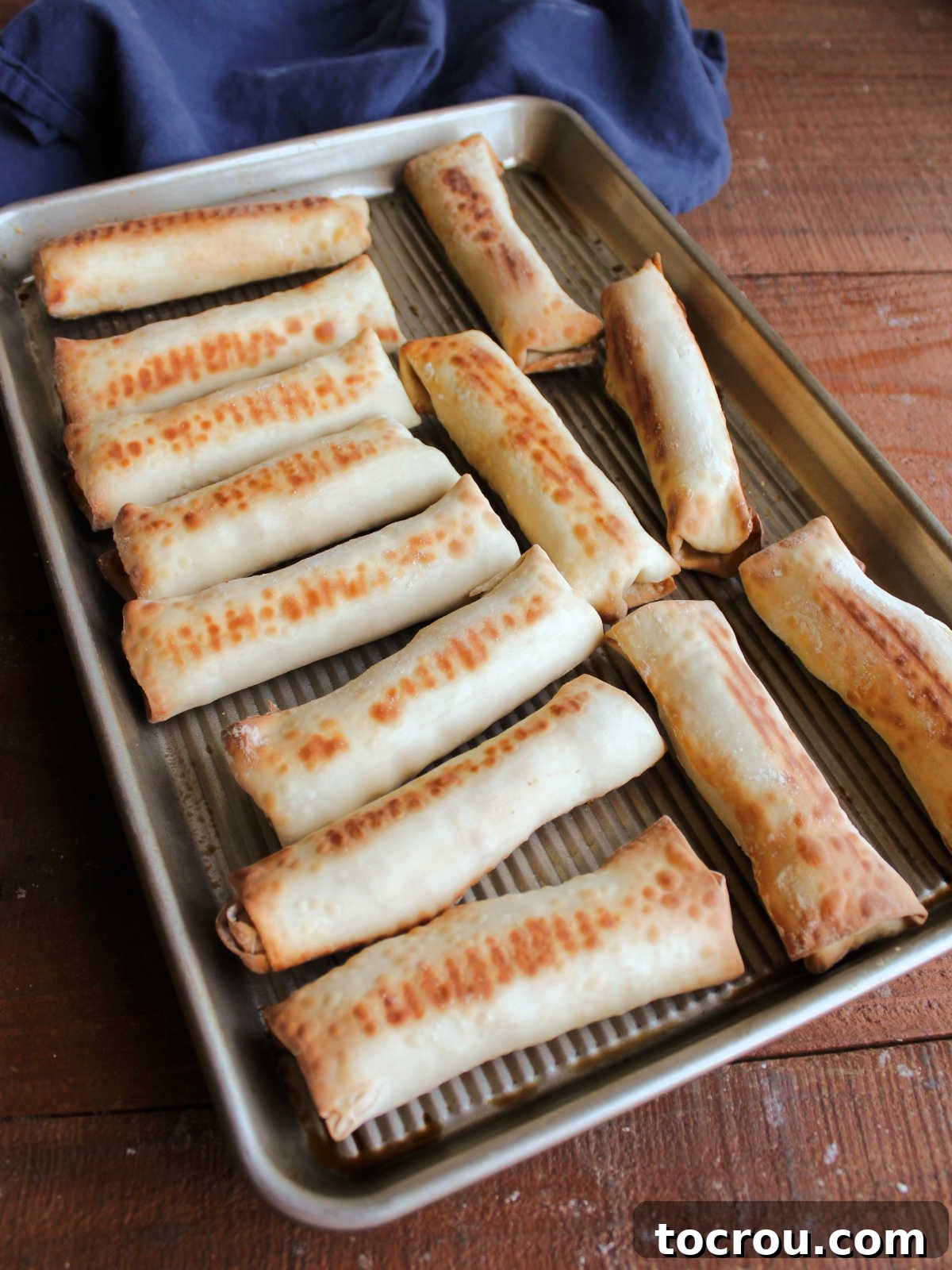Freshly Baked Crab Rangoon Egg Rolls Golden brown and crispy baked crab rangoon egg rolls, fresh out of the oven, on a baking sheet.