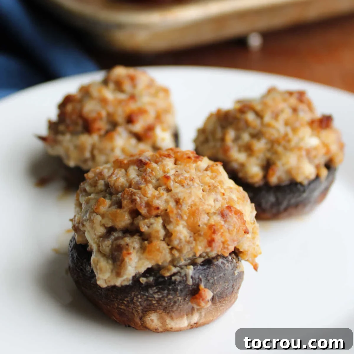 These creamy sausage filled stuffed mushrooms are always a hit. They are the perfect appetizer for a party or great for game day as well! Close up of baked stuffed mushrooms with sausage and cream cheese filling, golden brown and perfectly cooked.