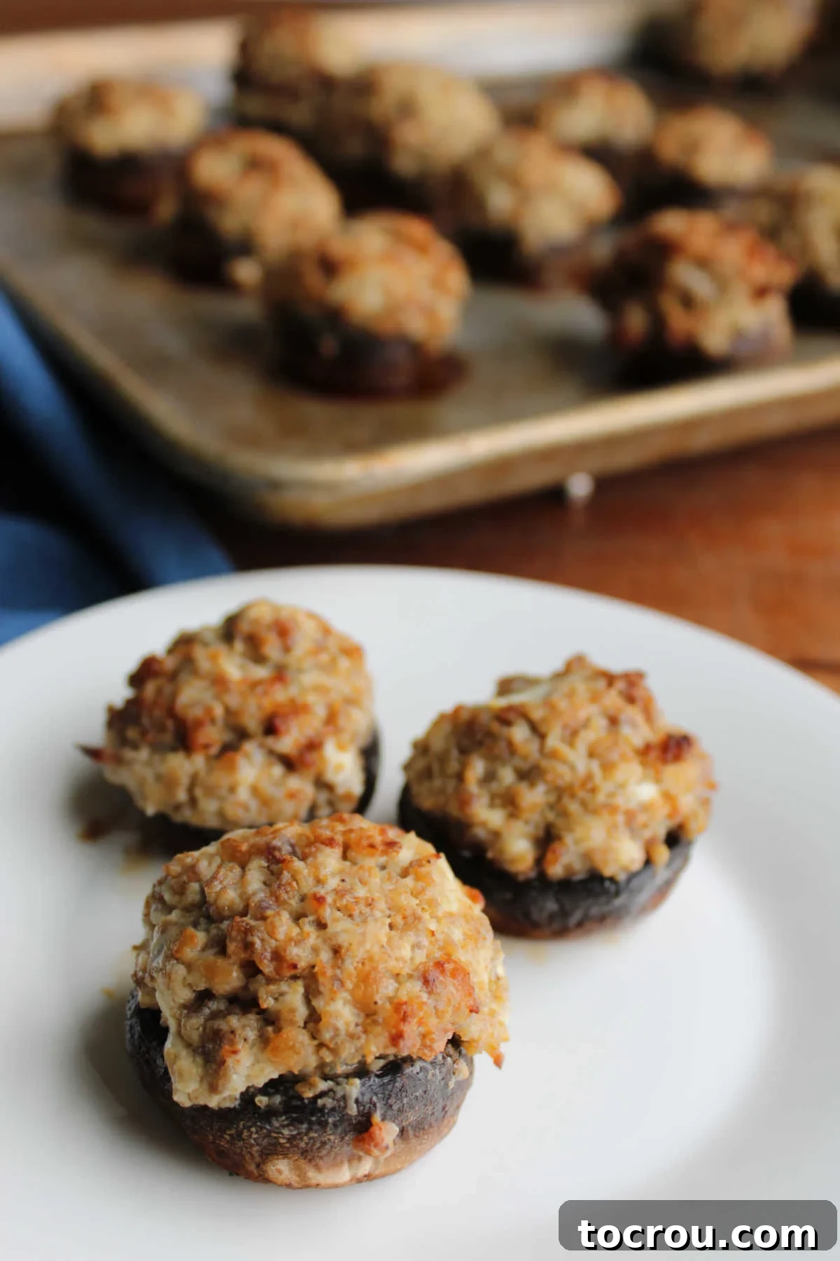 Savory Sausage Stuffed Mushrooms 6 Plate with sausage stuffed mushrooms in front of pan with remaining stuffed mushrooms.