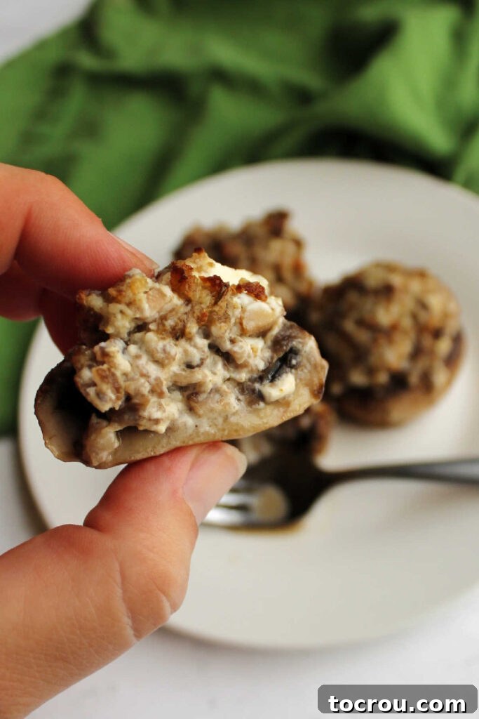 Savory Sausage Stuffed Mushrooms 7 Hand holding half of a sausage stuffed mushroom showing creamy filling.